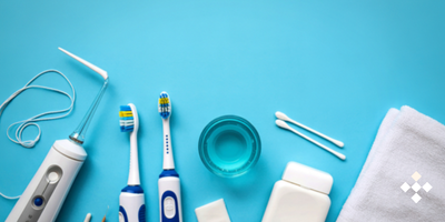 A collection of oral hygiene products including an electric water flosser, two toothbrushes, mouthwash, cotton swabs, a white towel, and a bottle on a blue background.